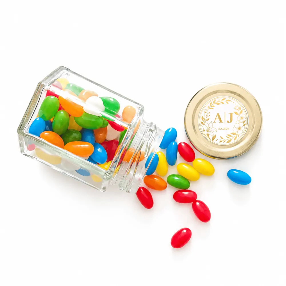 A clear glass jar with a gold lid filled with colorful jelly beans for monogram wreath wedding favours