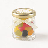 A clear glass jar with gold lid and cream ribbon bow filled with colorful gummies for monogram wreath wedding favours