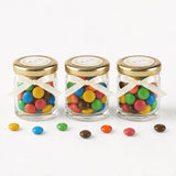 Three clear glass jars with gold lids ribbon bow filled with colorful mms wedding favours with monogram wreath foil stickers