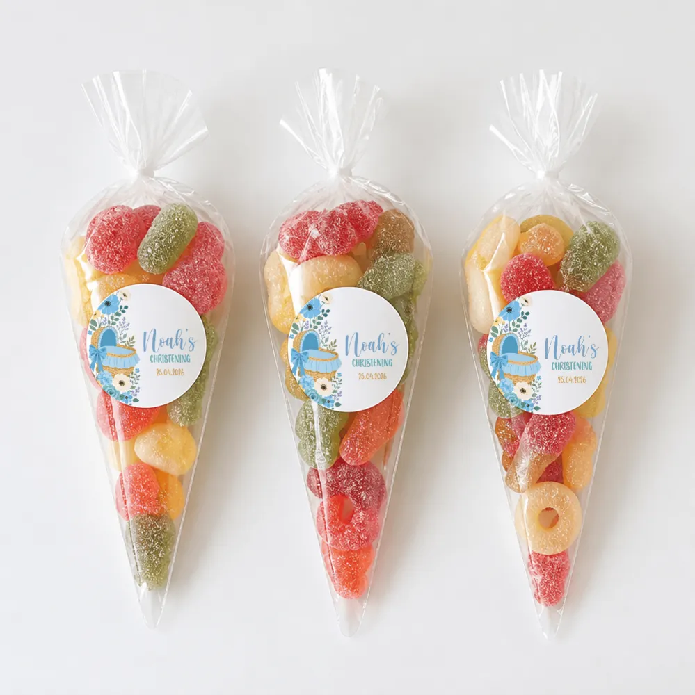 Three clear plastic sweet cones filled with colorful gummies and blue noah’s christening labels for moses basket gift