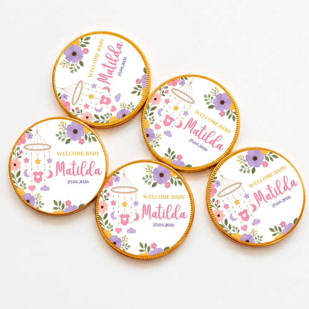 Round gold-edged milk chocolate coins with white center floral design and pink welcome baby matilda text for nursery mobile