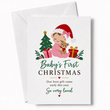 A white christmas card featuring a cartoon baby in pink pajamas and santa hat on 300gsm card titled our best gift came early