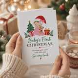 A white 300gsm christmas card featuring a cartoon baby in a red santa hat holding a teddy bear and gifts titled our best gift came early baby first christmas card