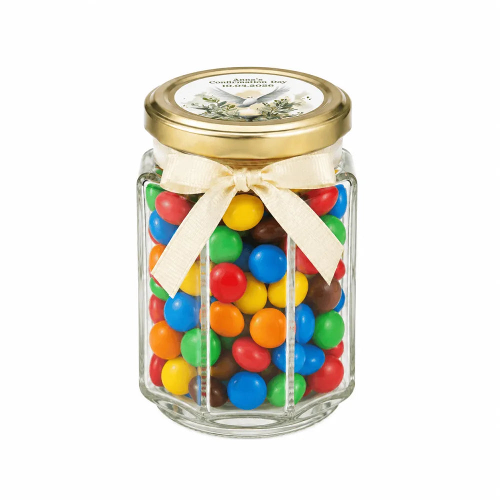 A clear hexagonal glass jar with a gold lid and cream bow filled with colorful mms in a peaceful dove confirmation favor