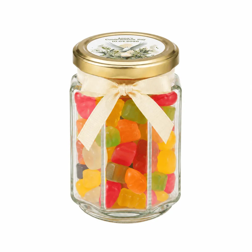 A clear glass hex jar favour with a pale gold twist lid and cream ribbon bow filled with colorful gummy bears