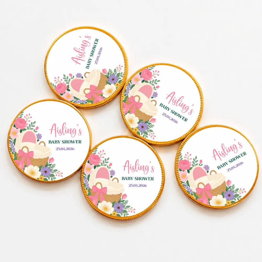 Round gold-edged chocolate coins with pink bassinet floral design and woven basket for baby shower favors