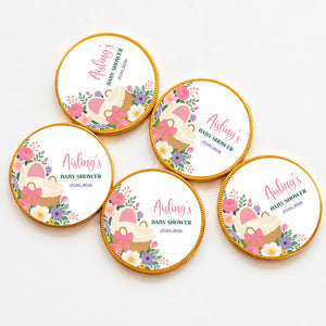 Round gold-edged chocolate coins with pink bassinet floral design and woven basket for baby shower favors
