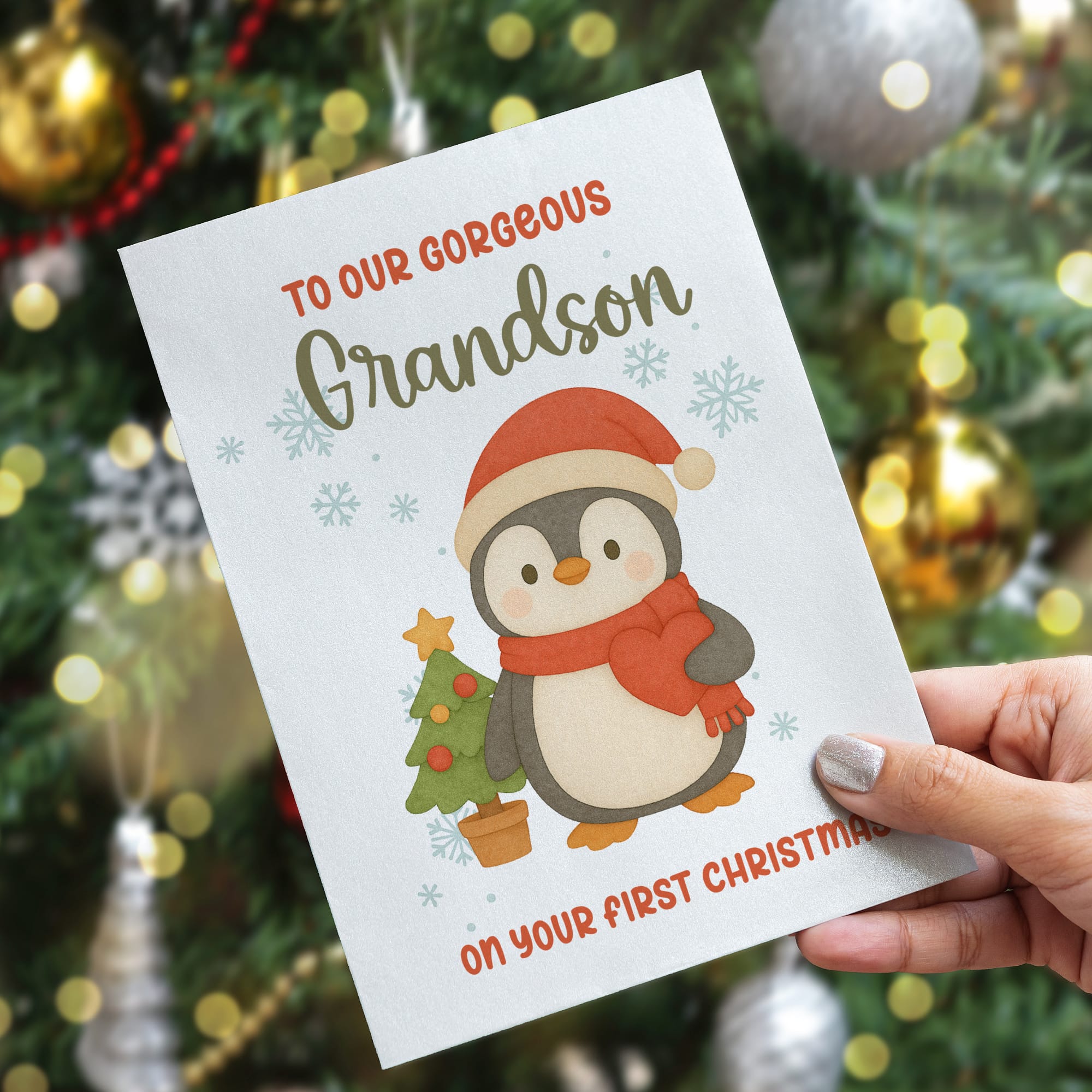 Christmas card with a penguin illustration and text held in front of a decorated Christmas tree.