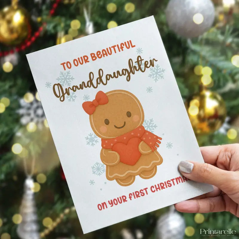 Greeting card for a granddaughter's first Christmas held in front of a decorated Christmas tree.