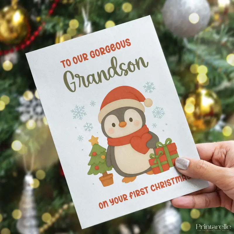 Card with a penguin illustration and text held in front of a decorated Christmas tree.