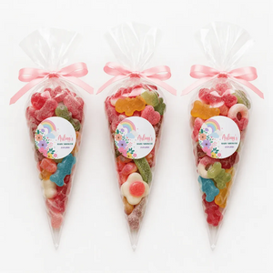 Three clear plastic sweet cones tied with pink ribbons and pastel rainbow labels for baby shower treats