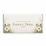 A personalised 40g chocolate bar wrapped in elegant foil with cream flowers green leaves and gold accents for weddings