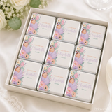 A white gift box of twelve mini neapolitan chocolates wrapped with illustrations of baby elizabeth in lavender swaddle