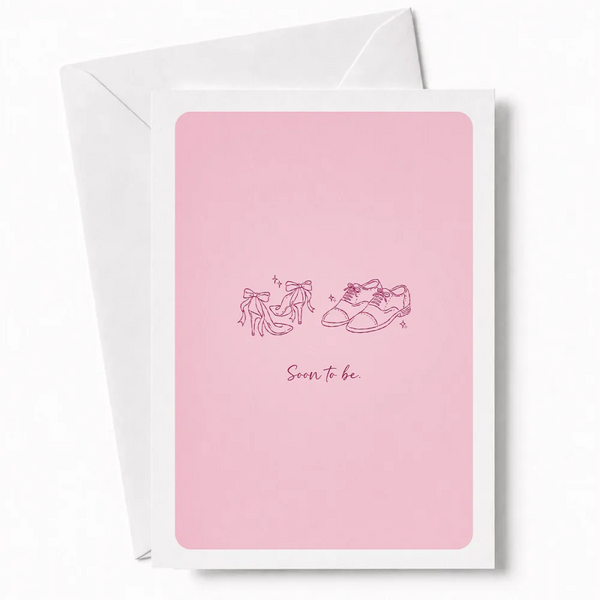 Pink engagement card with minimalist line drawing of bridal heels and groom’s oxford shoes on front