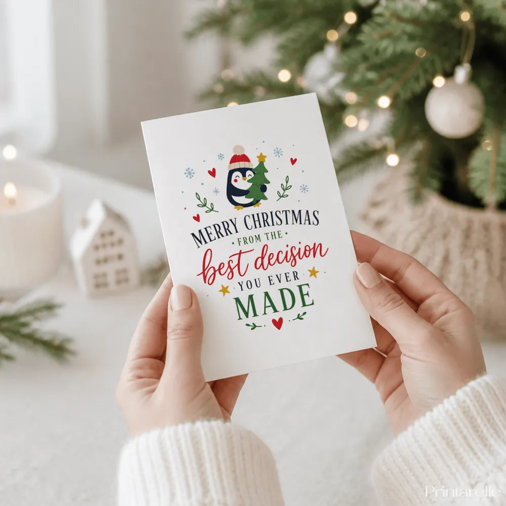 A white penguin christmas card with a cartoon penguin in a red hat holding a tree and best decision text