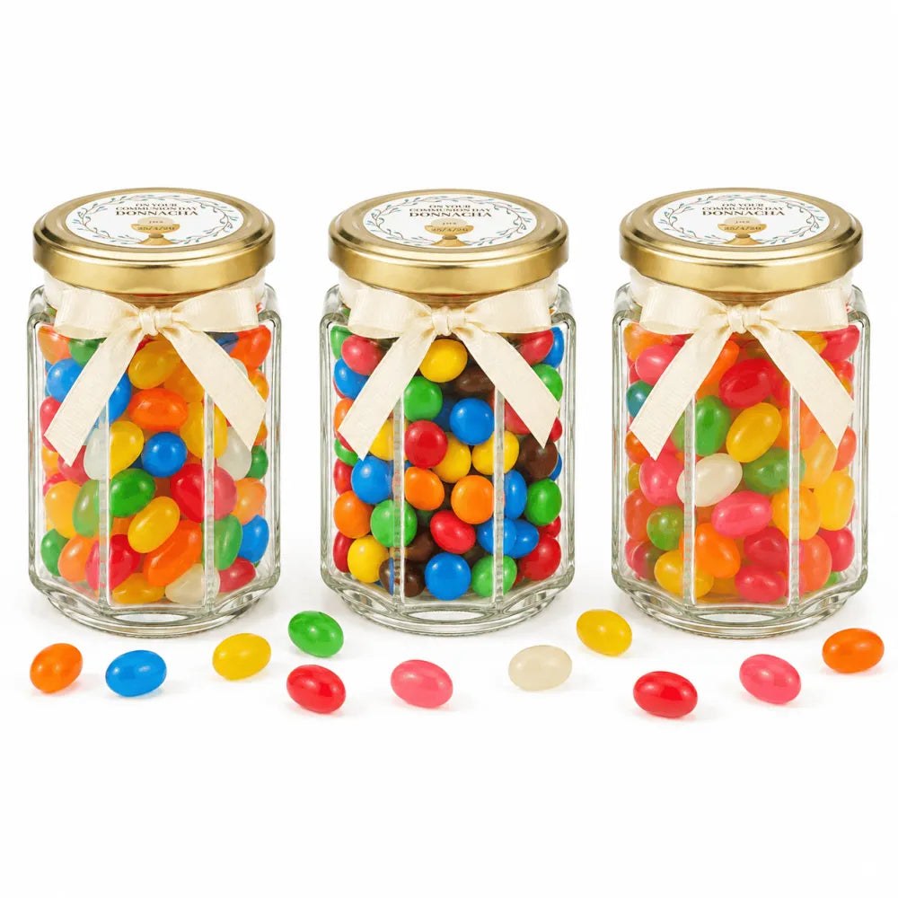 Three hexagonal glass jars with gold lids and cream ribbons filled with jelly beans and personalised 48mm pale gold sticker