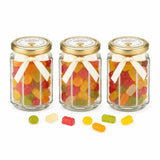 Three hexagonal glass jars with pale gold twist lids and cream bows filled with gummy sweets with personalised sticker