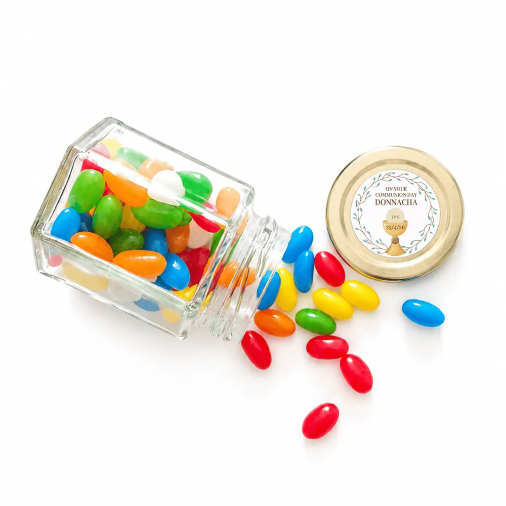 A clear 106ml glass jar tipped over spilling colorful jelly beans with a 48mm pale gold twist lid and personalised sticker