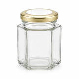 Clear hexagonal glass jar with pale gold twist lid and 48mm pale gold personalised sticker for sweets party favors