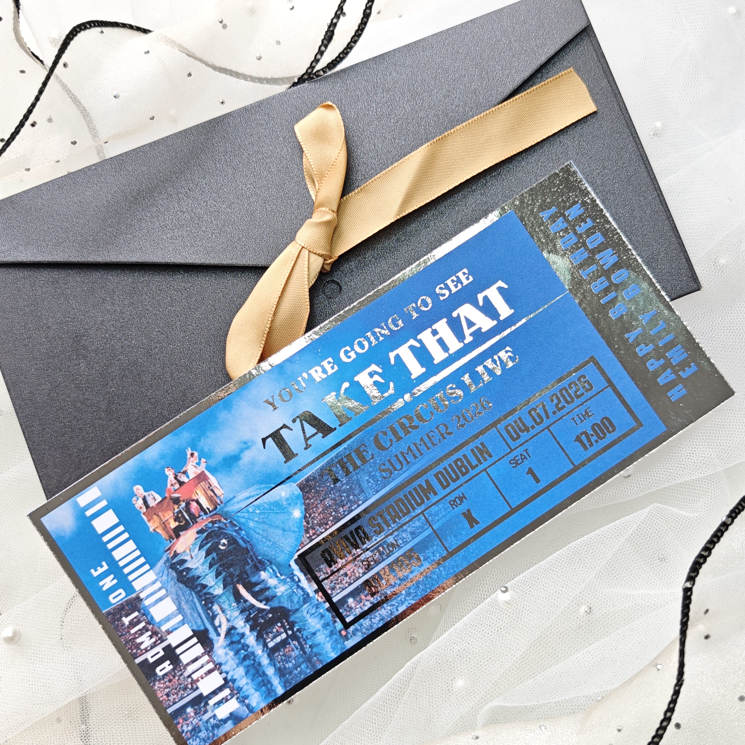 Promotional ticket for 'Take That' circus live event with a gold ribbon on a white background