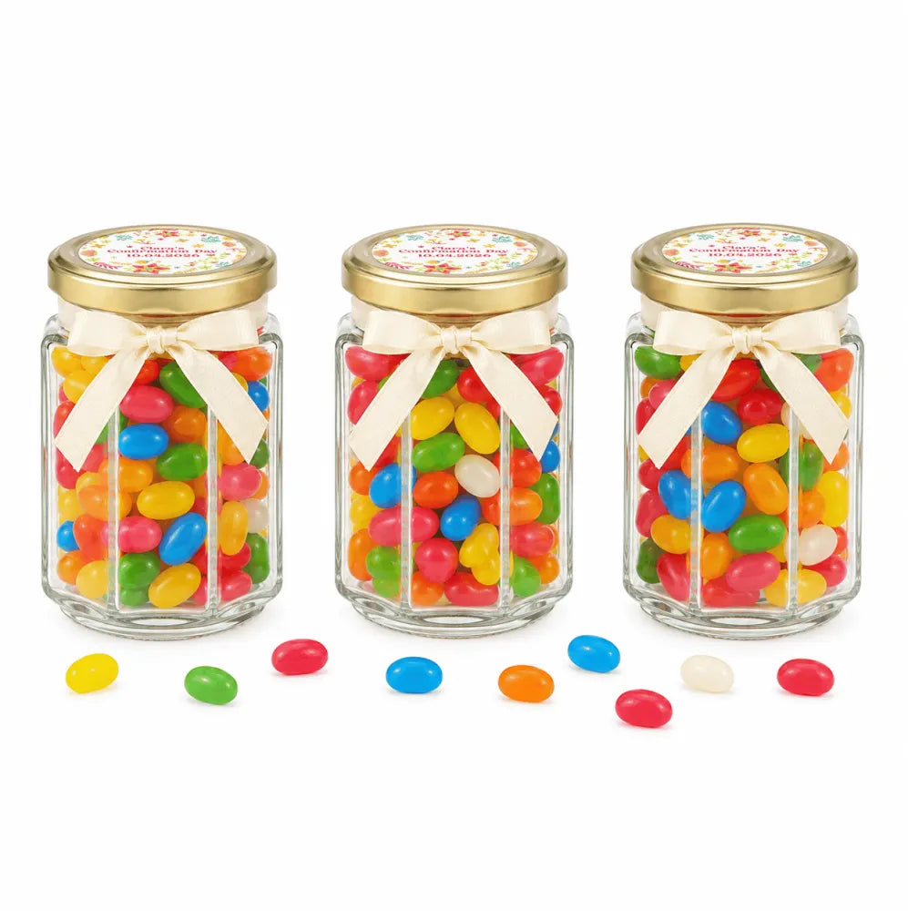 Three clear glass wildflower blessing hex jars with 48mm pale gold twist lids, cream ribbons, and personalised sticker printed labels filled with colorful jelly beans
