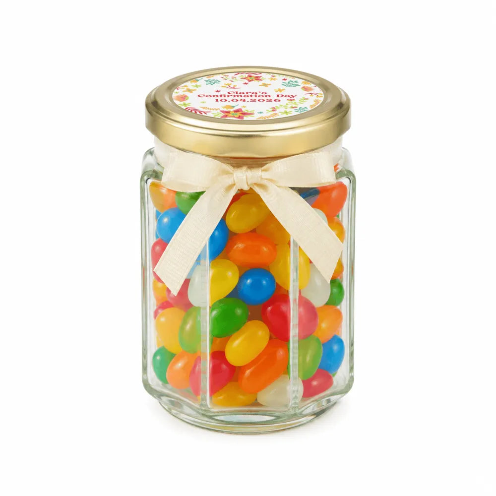 A clear glass hex jar favour filled with colorful jelly beans and a 48mm pale gold twist lid with cream ribbon bow
