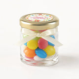 A personalised mini jar favour filled with colorful jelly beans in a clear glass jar with 43mm pale gold lid and cream bow